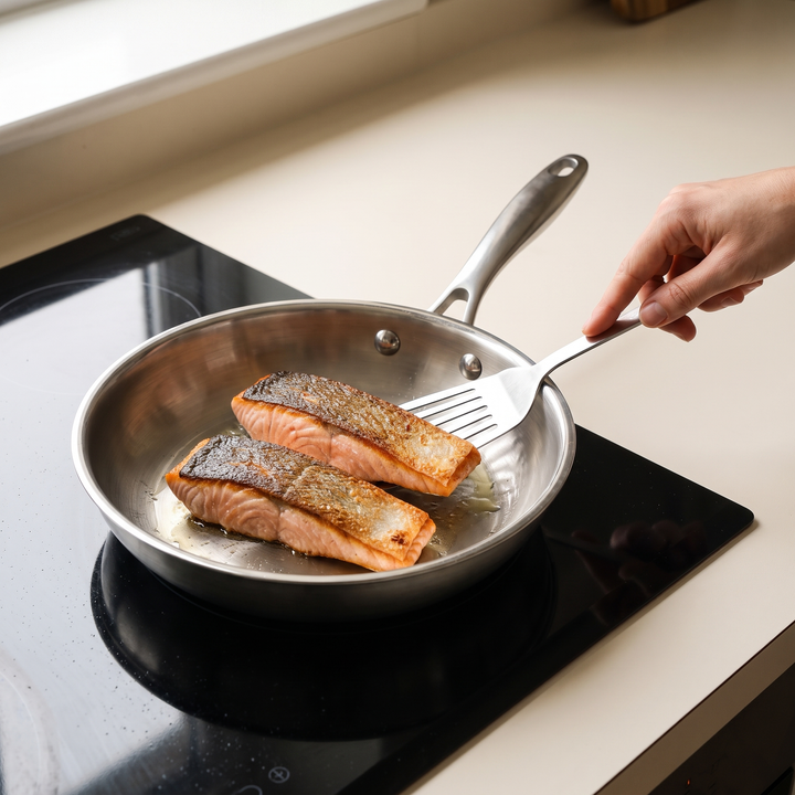 Deux pavés de saumon saisis côté peau dans une poêle inox, peau dorée et croustillante