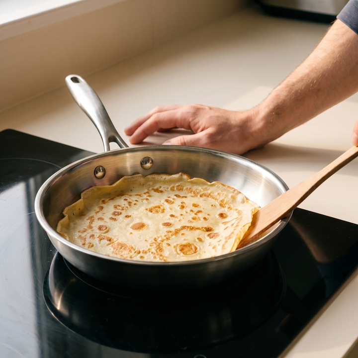Crêpe dorée cuisant dans une poêle inox, les bords qui se soulèvent seuls
