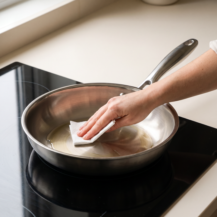 Film d'huile étalé au papier absorbant dans une poêle inox chaude, sur plaque à induction