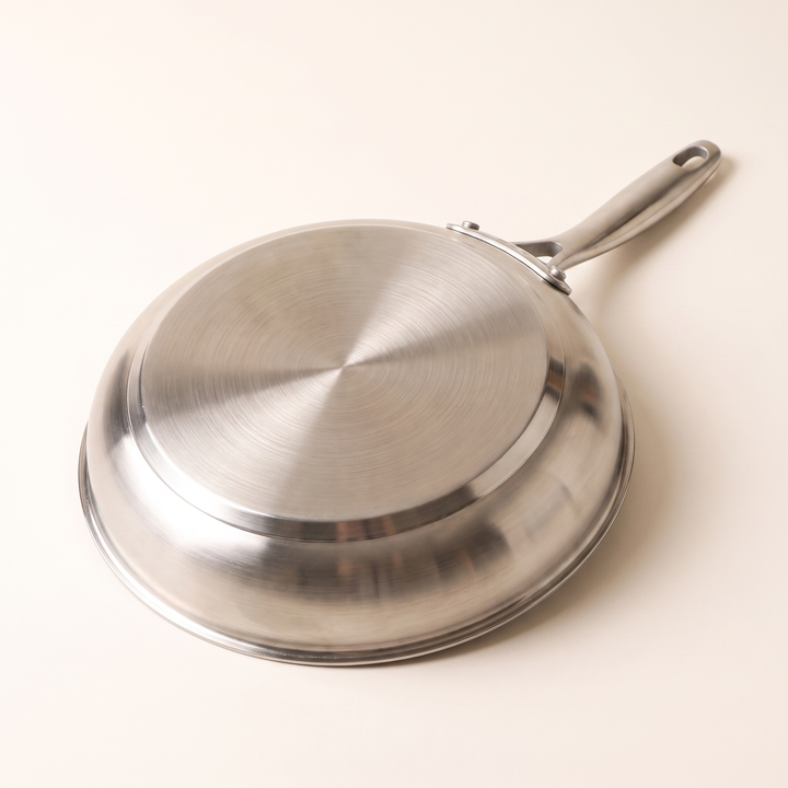 Dessous d'une poêle inox retournée montrant le fond plat magnétique compatible induction