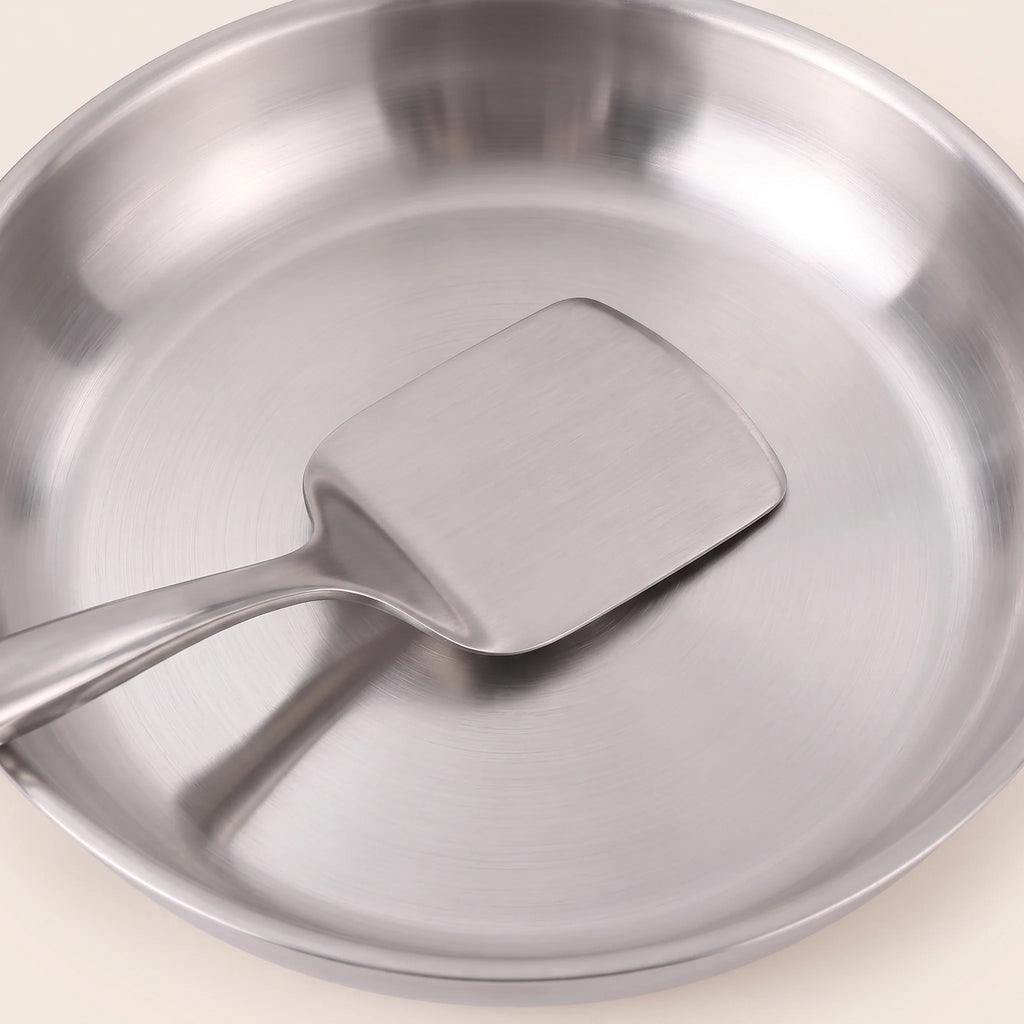 Gros plan sur le fond d'une poêle de la batterie 11 pièces, une spatule en inox posée dedans