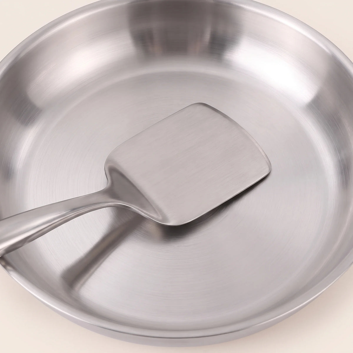 Gros plan sur le fond d'une poêle de la batterie 11 pièces, une spatule en inox posée dedans