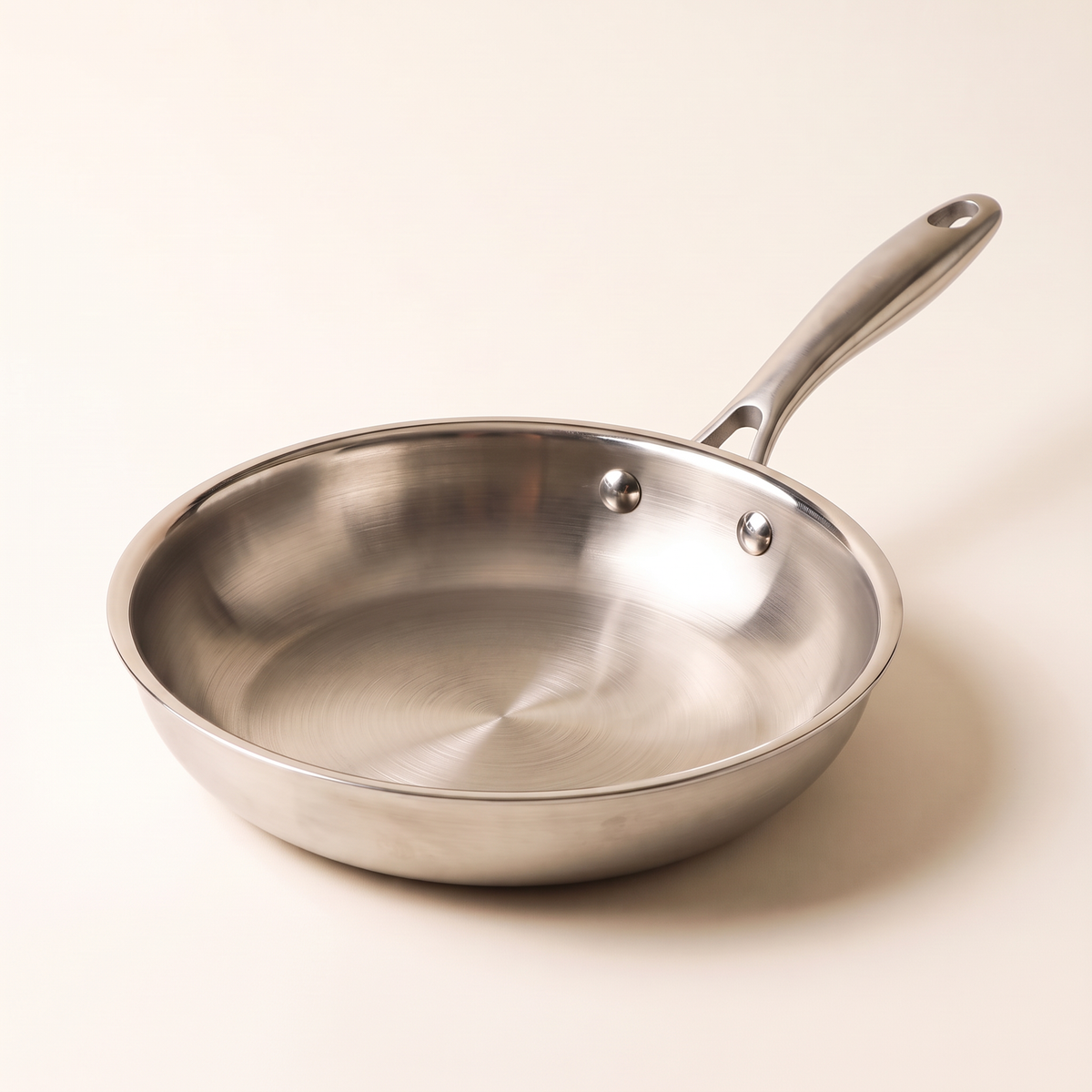 Poêle inox 22 cm Marthe vue de trois quarts, manche riveté, fond blanc beurre