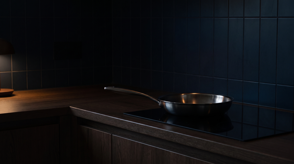 La sartén de acero inoxidable Marthe sobre la placa de inducción de una cocina oscura con azulejos azul noche