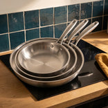 Les trois poêles inox Marthe emboîtées sur une plaque à induction, cuisine en chêne et zellige bleu